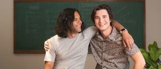 Two people sitting with their arms over one another's shoulders