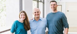 Three people standing with their arms around one another's backs